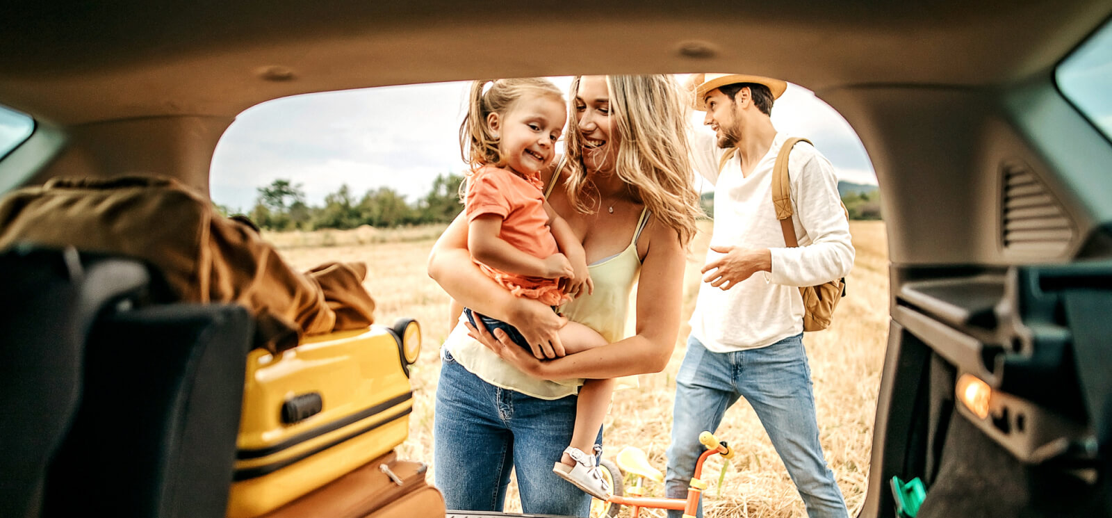 A young family looking into the back trunk of a car