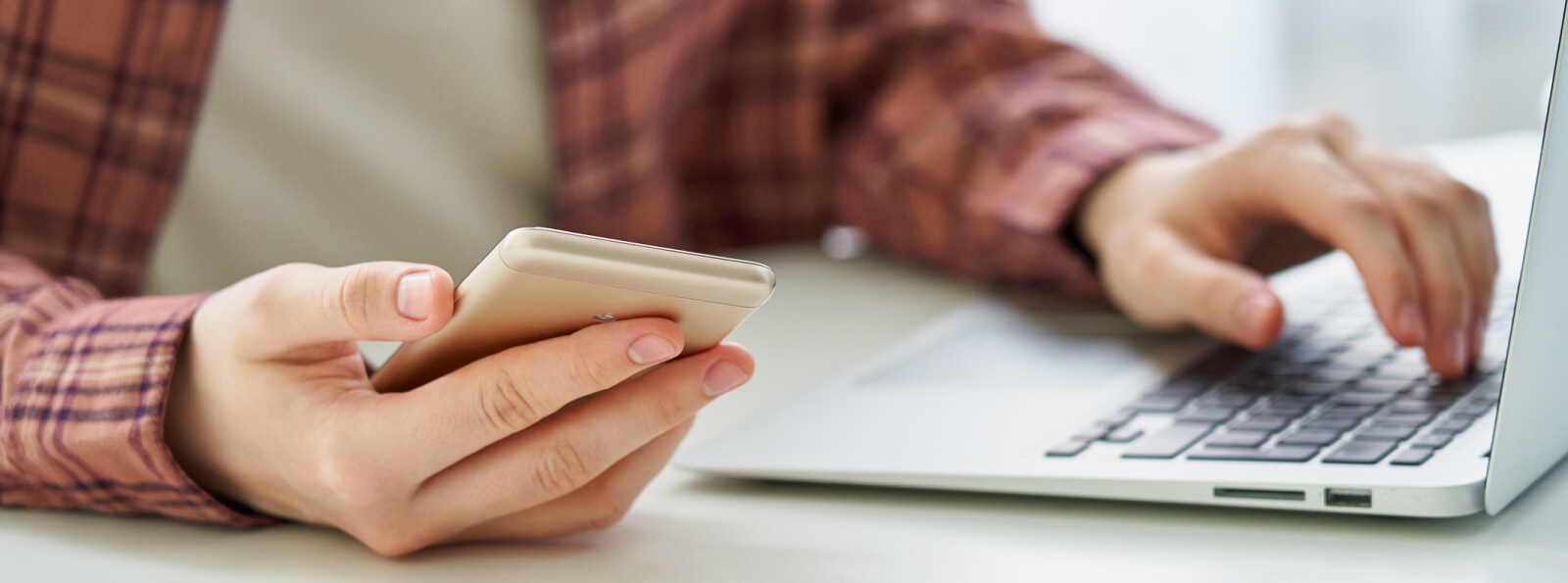 Close up of a person's hand holding a smartphone and using a laptop